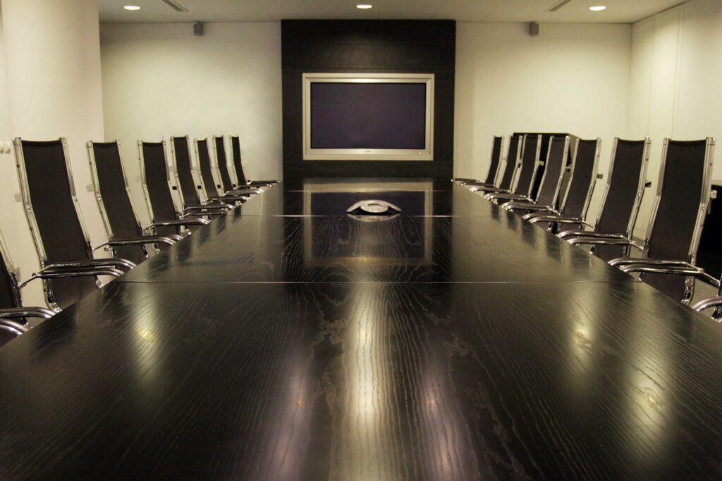 Modern boardroom with a long polished conference table, executive chairs, and a large display screen